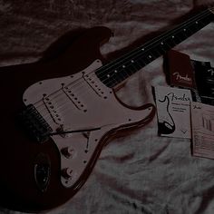 an electric guitar sitting on top of a bed next to a book and some papers