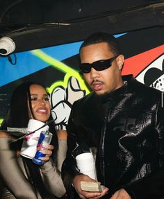 a man and woman standing next to each other in front of a graffiti covered wall