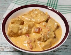 a white bowl filled with meat covered in gravy on top of a wooden table