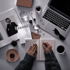 a person is writing on a book while sitting at a desk with other items around them