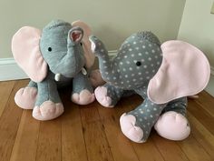 two stuffed elephants sitting next to each other on a wooden floor