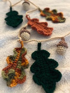 crocheted leaves and acorns are hanging on a white tablecloth with twine