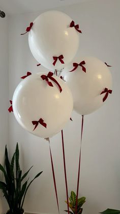 three white balloons with red bows on them are in the air next to a potted plant