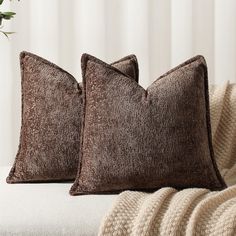 two brown pillows sitting on top of a white couch next to a vase with flowers