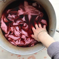 a woman's hand reaching into a pot filled with red cloth