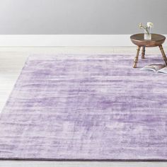 a purple rug in the middle of a room with a coffee table and flower vase