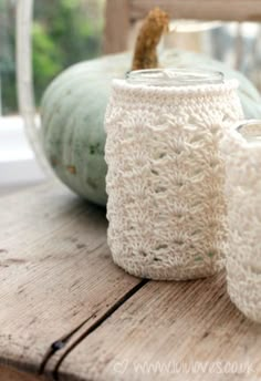 two white crocheted jars sitting on top of a wooden table next to pumpkins