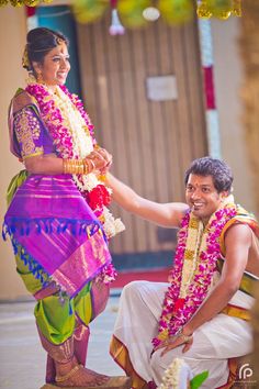 a man kneeling down next to a woman in a purple and green sari on her wedding day