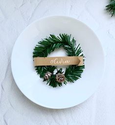 a white plate topped with pine cones and a wooden name tag next to evergreen branches