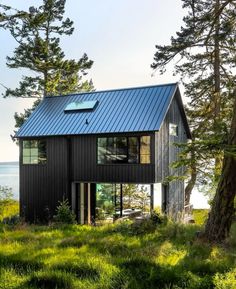 a black house sitting on top of a lush green hillside next to the ocean and trees