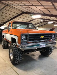 an orange truck parked in a garage next to a white and black car with large tires