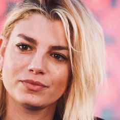 a close up of a person with blonde hair and piercings on her ear, looking at the camera