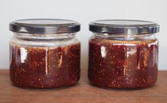 two jars filled with red sauce sitting on top of a wooden table