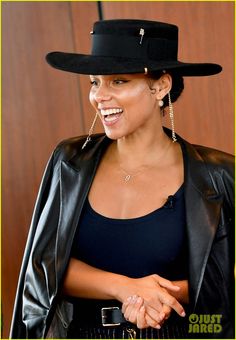 a woman wearing a black hat and leather jacket smiling at the camera with her hand on her hip