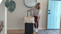 a woman standing next to a bag of luggage in front of a mirror and door