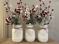 three white mason jars with red and white flowers in them are sitting on a table