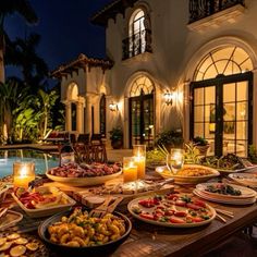 a table full of food next to a swimming pool at night with candles on it