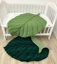 a white crib with a green blanket on top of it and a large leaf shaped pillow in the middle