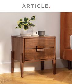 a wooden table with two drawers and a cup on it next to a plant in a white vase