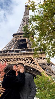 a man and woman standing in front of the eiffel tower, kissing each other