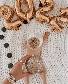 a woman laying on top of a white blanket next to gold foil balloons and numbers