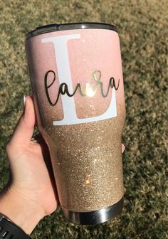 a hand holding a pink and gold glittered tumbler with the letter d on it