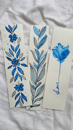 three blue flowers and leaves painted on white paper next to each other with watercolor pencils