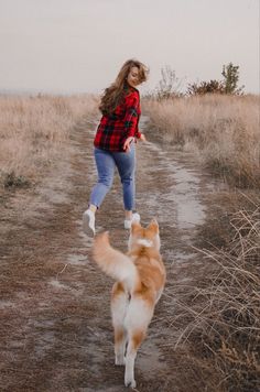 a woman is playing with her dog in the middle of a dirt road on a cloudy day