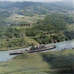 an aerial view of a large ship in the middle of a river surrounded by green hills