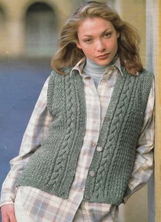 a woman wearing a green vest and plaid shirt standing in front of a wall with her hands on her hips