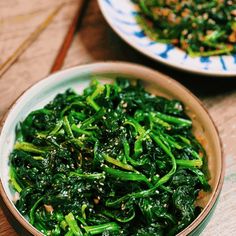 two bowls filled with green vegetables on top of a wooden table next to another bowl