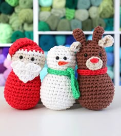 three crocheted snowmen are standing next to each other in front of yarn balls