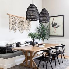 a dining room table with chairs and a bench in front of it, along with hanging art on the wall