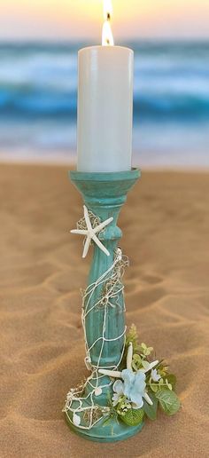 a candle is sitting on the sand at the beach with flowers and starfish around it