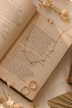 an open book with two necklaces on top of it next to flowers and a pocket watch