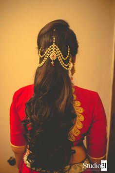 a woman with long hair wearing a red blouse and gold head piece, standing in front of a wall