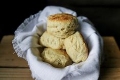 some biscuits are sitting in a white bowl on a wooden table with a cloth around it