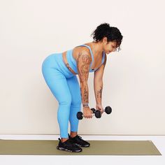 a woman in blue leggings lifts two dumbbells while looking down at her stomach