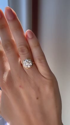 a woman's hand with a diamond ring on her finger, next to a window