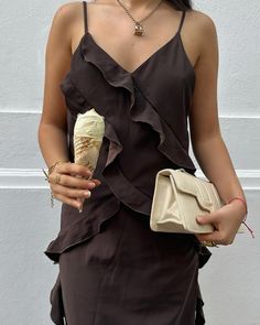 Close-up of a woman in a black ruffled dress holding an ice cream cone and a cream bag.