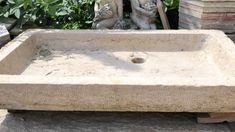 a stone sink sitting in front of some plants and trees with a statue on top