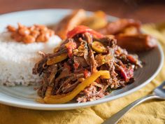 a white plate topped with meat and vegetables next to rice on top of a yellow table cloth