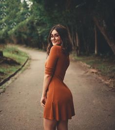 a woman in an orange dress is standing on a path and smiling at the camera