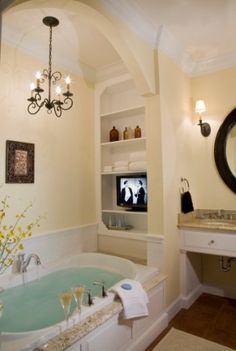 a bath tub sitting under a bathroom mirror next to a tv mounted on a wall