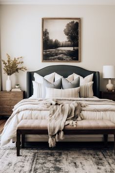 a bedroom with a large bed covered in white blankets and pillows next to a painting on the wall