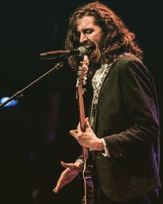 a man singing into a microphone while holding a guitar in his right hand and wearing a suit