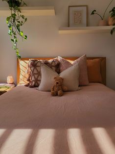 a teddy bear sitting on top of a bed in a room with plants and pillows