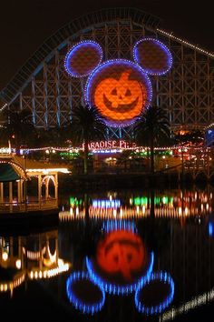 an amusement park at night lit up with lights and mickey mouse head on the front