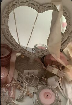 a heart shaped mirror sitting on top of a table next to other jewelry and candles