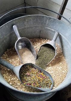 two metal scoops filled with different types of spices and herbs in a gray bucket